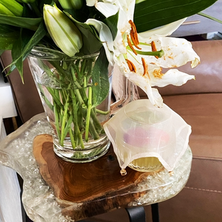 Silk cocktail veil with intricate hand-stitching, elegantly covering a glass sitting next to a glass pitcher used as a vase to contain white Casablanca lilies, atop a barstool made of wood and glass, nestle next to leather chair, ensuring a sophisticated and secure drinking experience