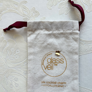 linen duster branded with Glass Veil logo and a handstitched butterfly charm laid out atop of wallpaper
